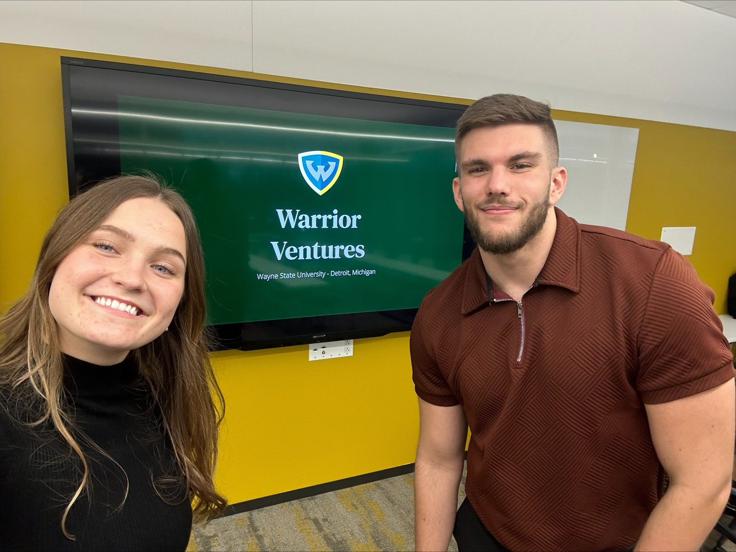 Man and woman smiling next to a screen that reads Warrior Ventures