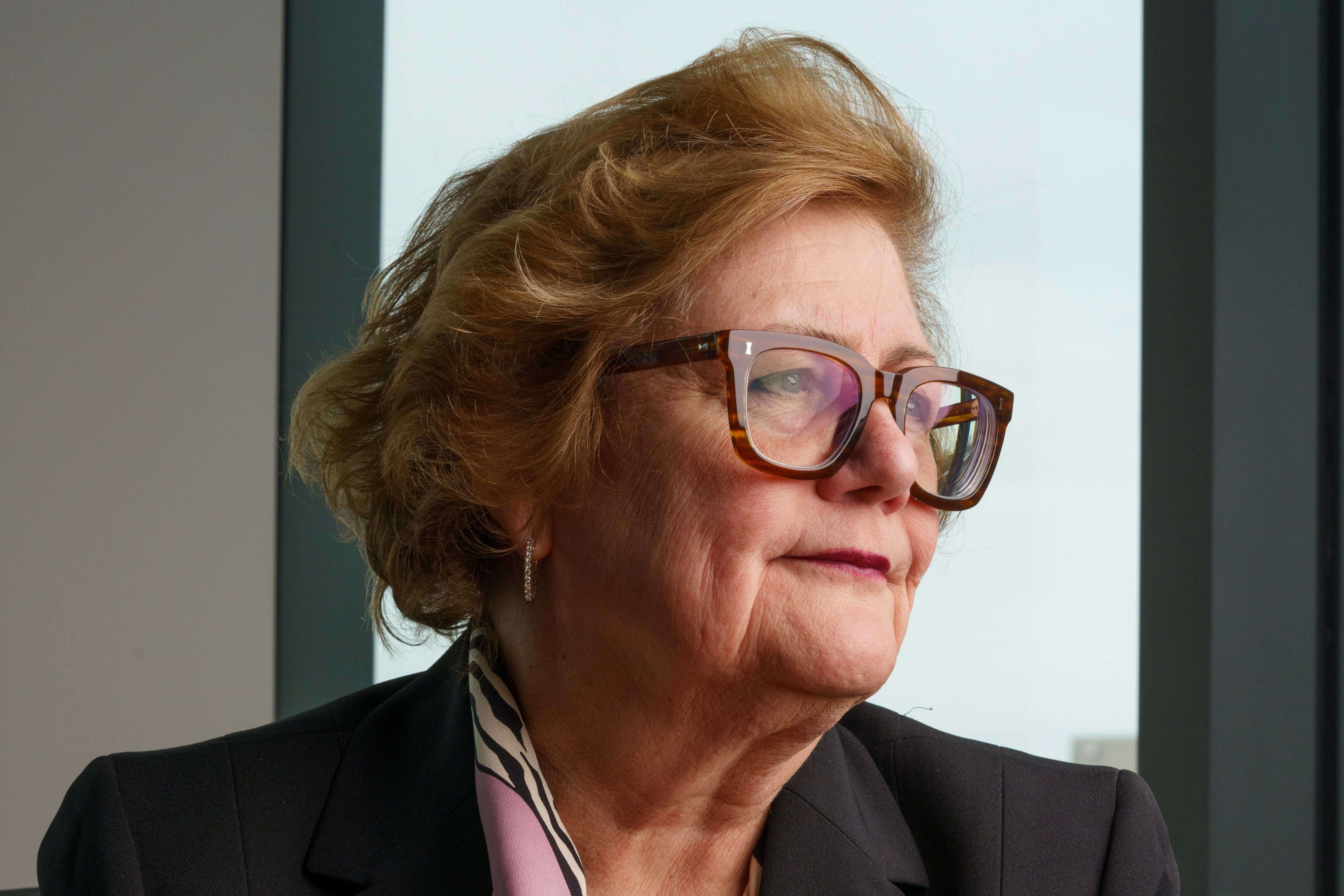 Dean Kleist sits at a table with her hands crossed and looking to her left, posing for an indoor headshot