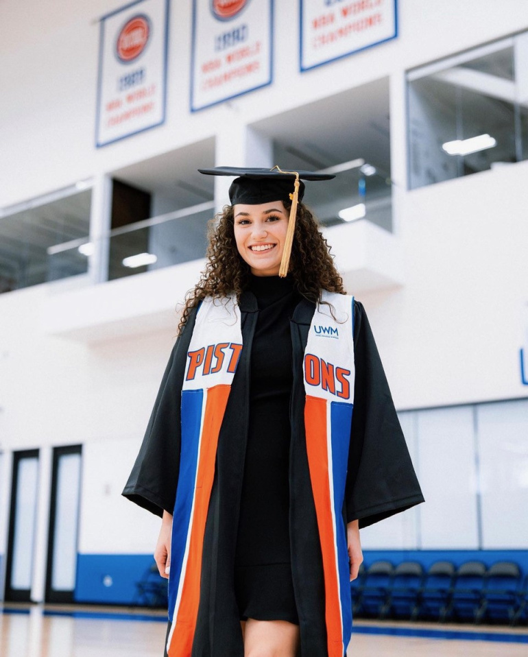 Ilitch School of Business alum Jenae Lodewyk wears a graduation cap and gown and a stole for the Detroit Pistons