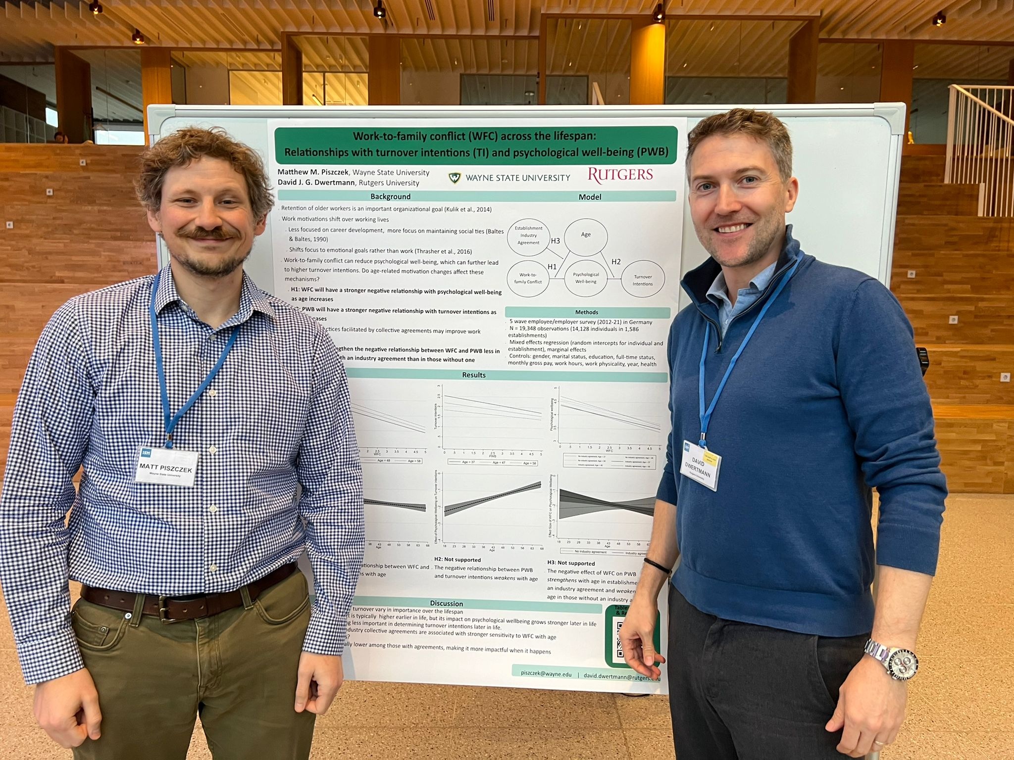 Two men stand in front of a poster presenting research