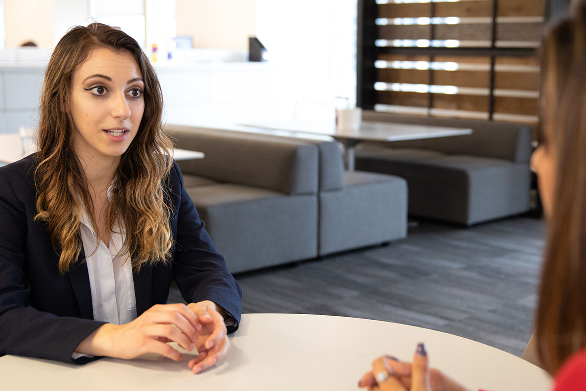 A female business student and female Ilitch School staff member sit at a table together having a conversation