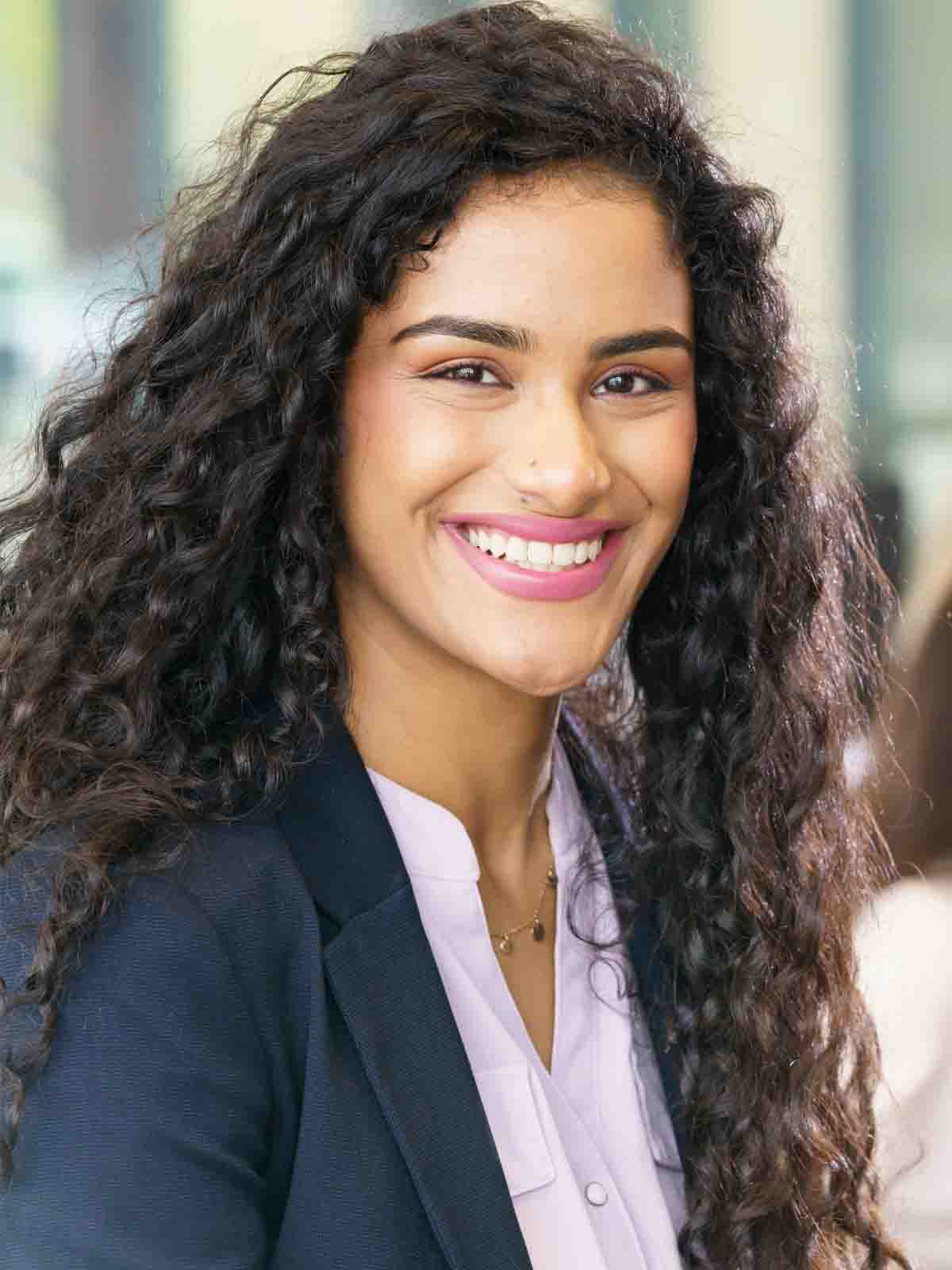 A female graduate business student smiles for a headshot with three other business students in the background