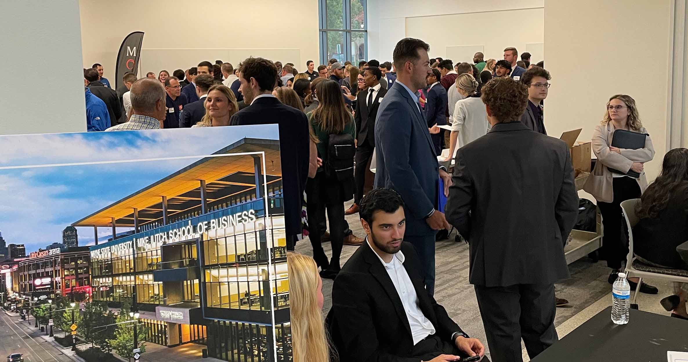 Ilitch School students sit and stand by a sign that says &quot;Supply Chain Networking Reception&quot; at a GSCM career networking fair