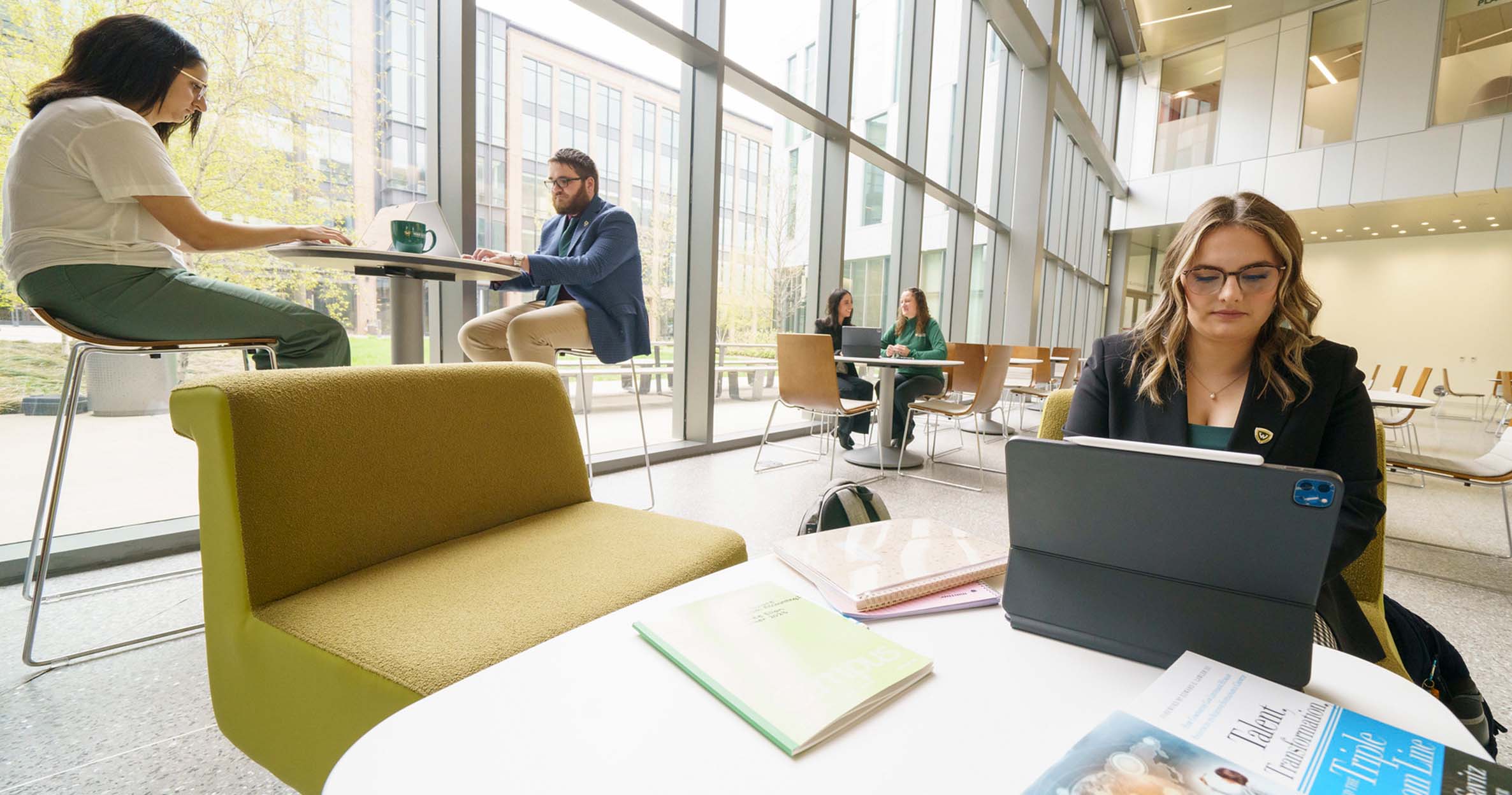 MBA students at the Mike Ilitch School of Business sit around tables in the lobby to talk and study