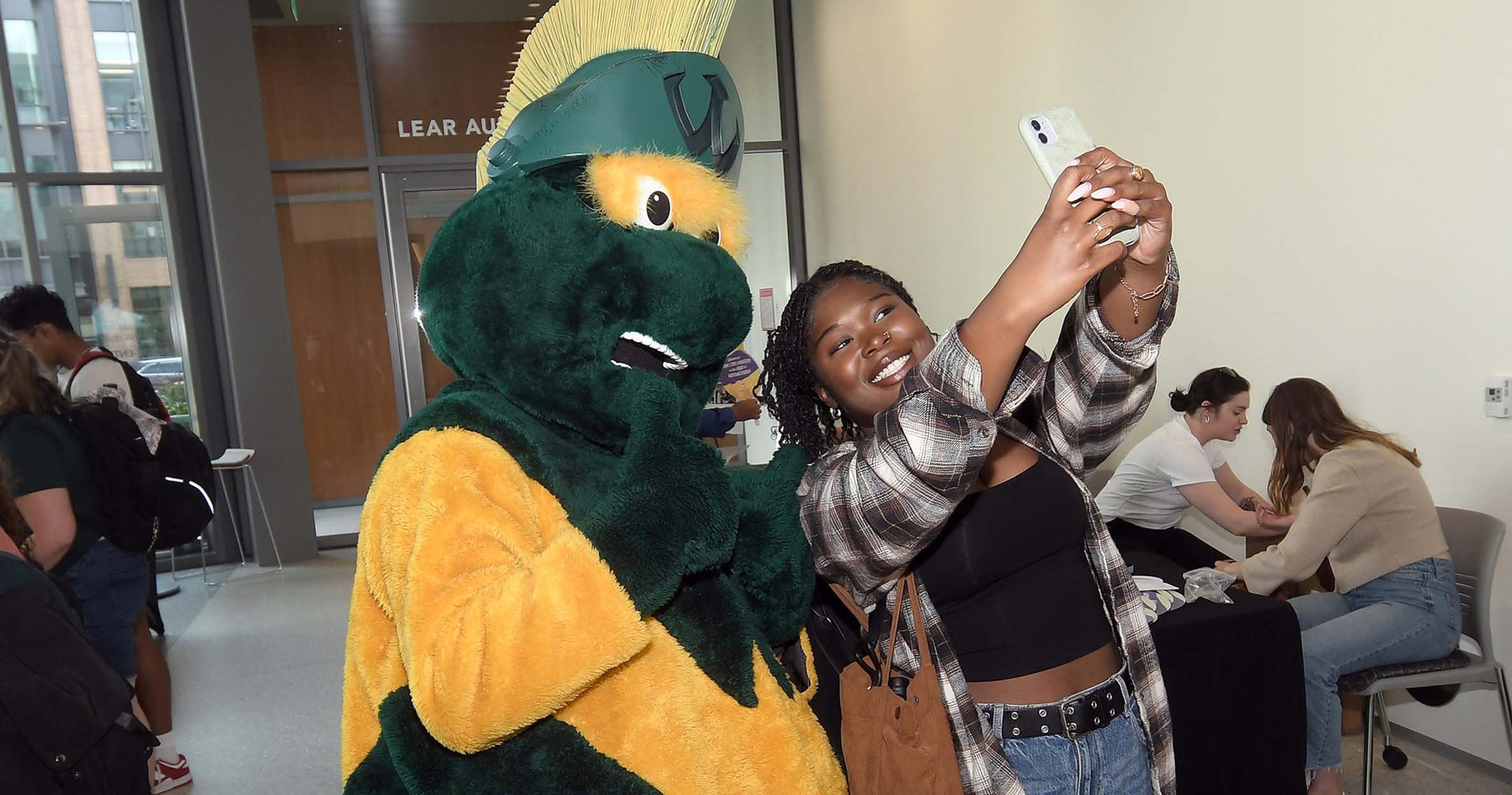 A female business student uses her phone to take a self-photo with WSU&#039;s mascot, W the Warrior