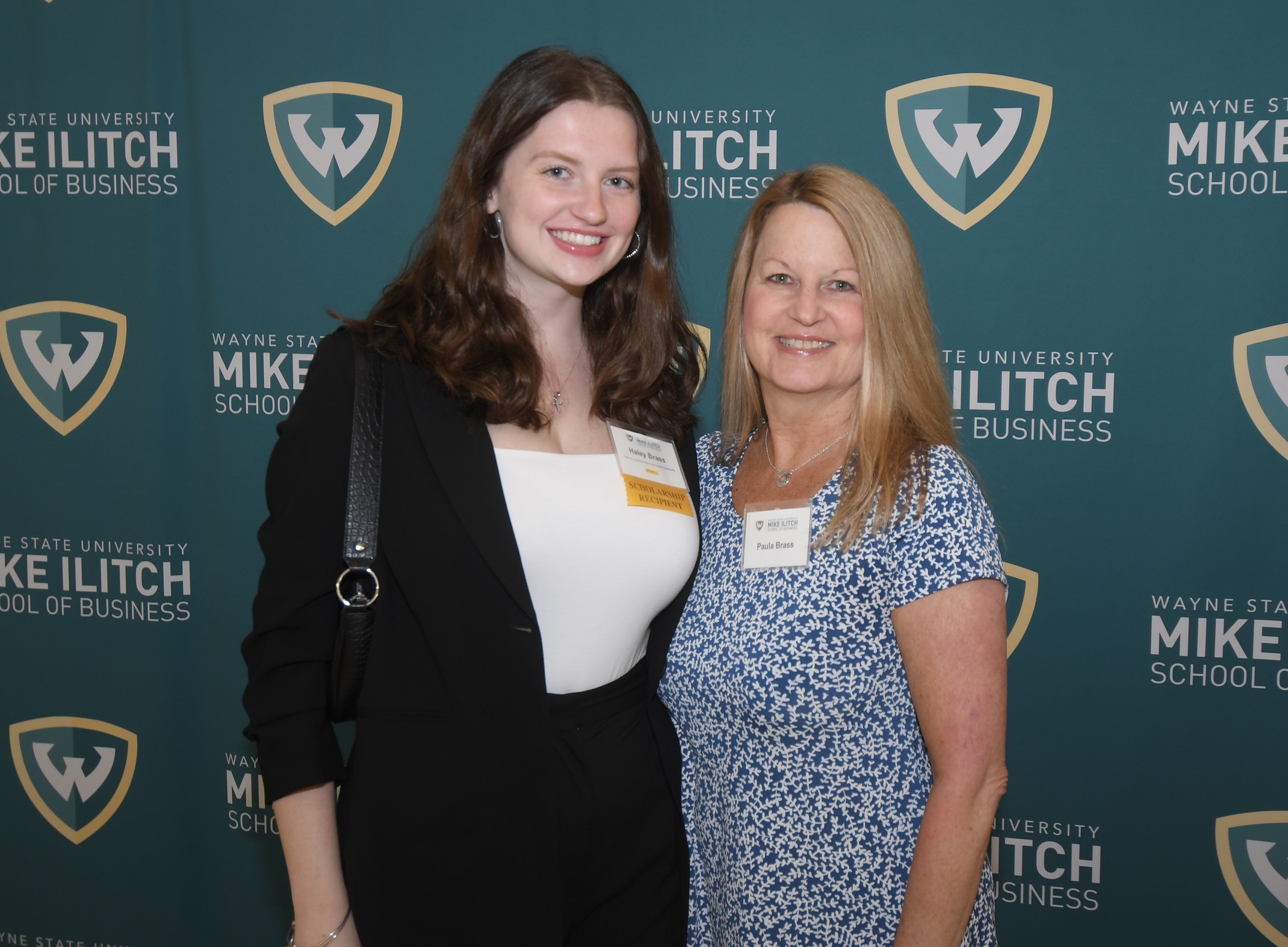 Haley and Paula Brass smile with their arms around each other in front of a WSU backdrop at an Ilitch School scholarship event