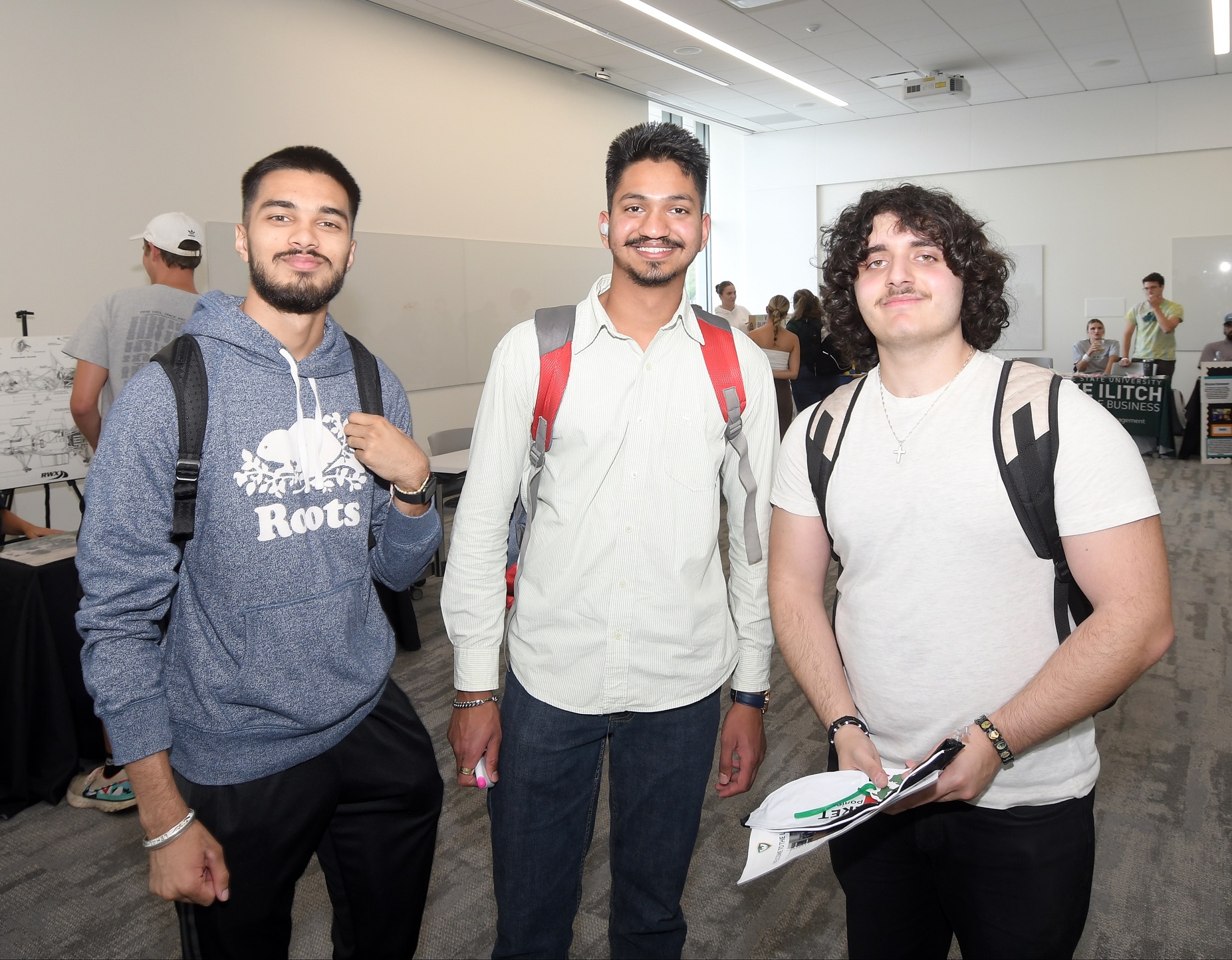 Three male business students wearing backpacks smile together while at an Ilitch School career fair