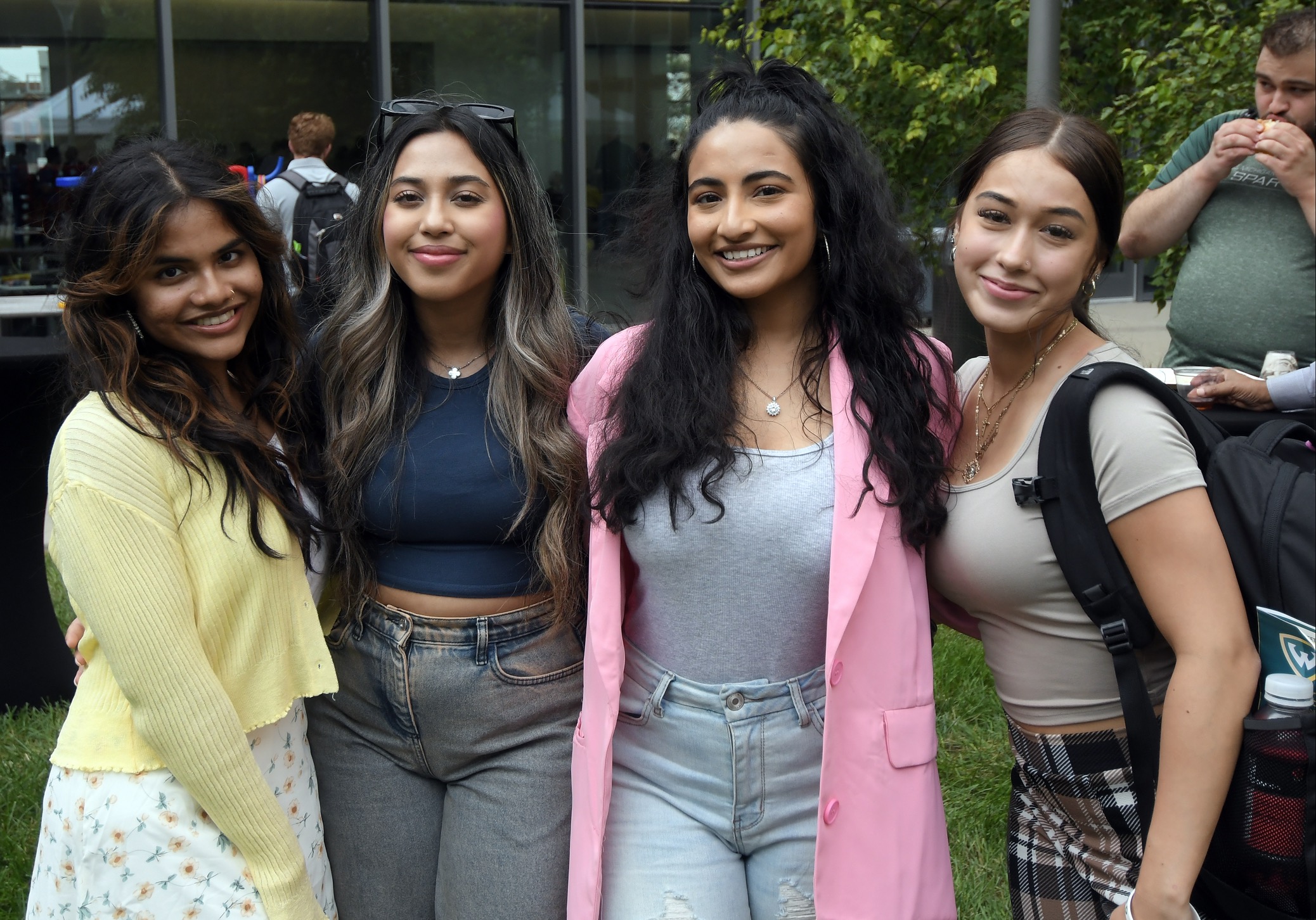 Four female business students smile and pose outside with their arms around each other