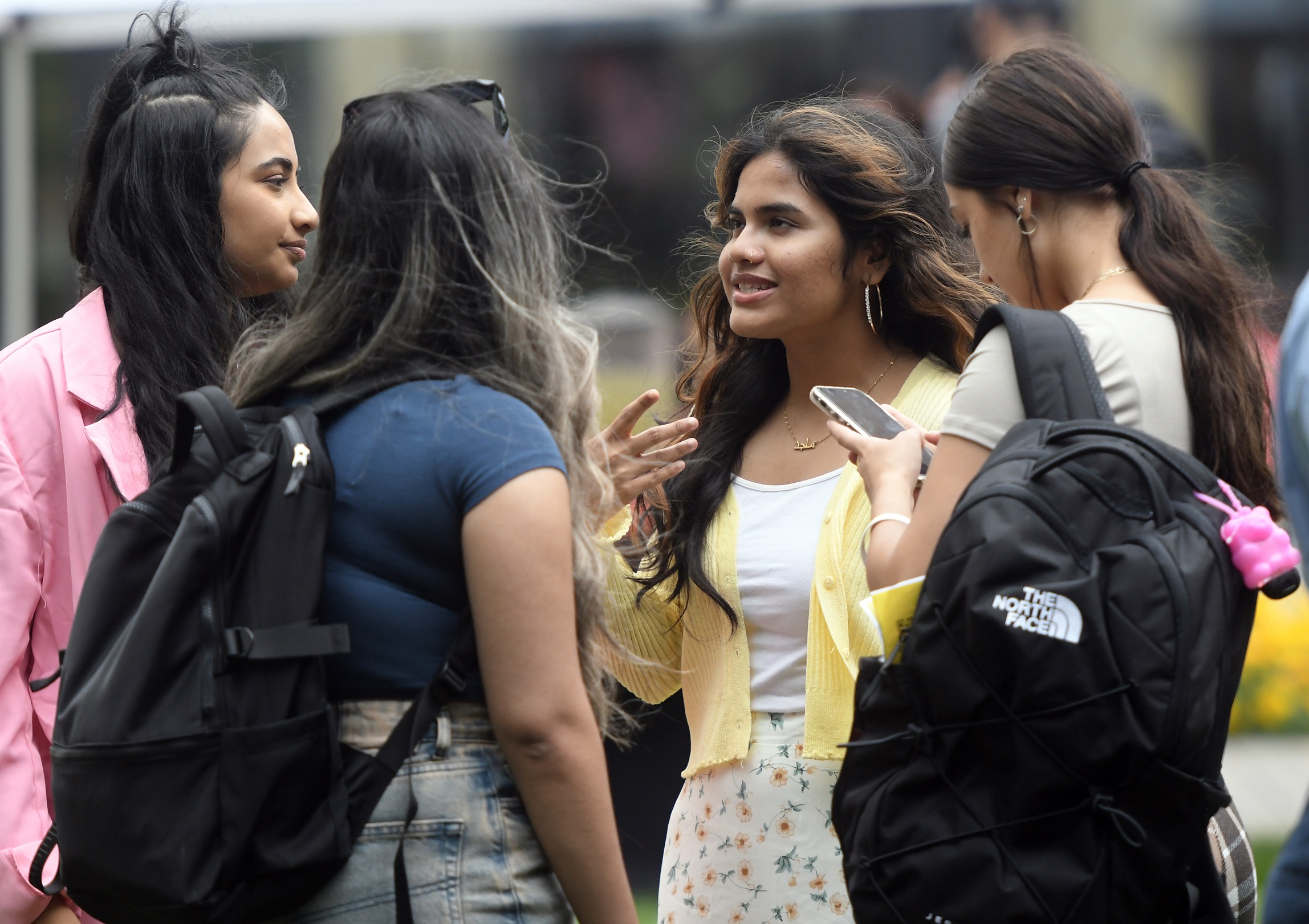 A group of four female business students, with one looking at her cell phone, stand outside talking to one another