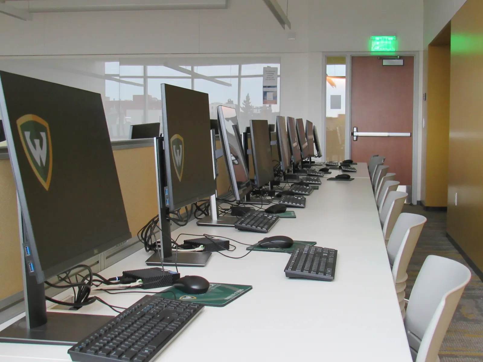 A row of nine desktop computers with the WSU logo on them in an Ilitch School of Business computer lab