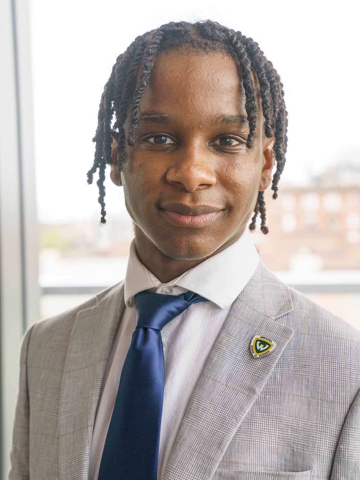 A male graduate business student wearing a suit, tie and WSU pin poses for an indoor headshot