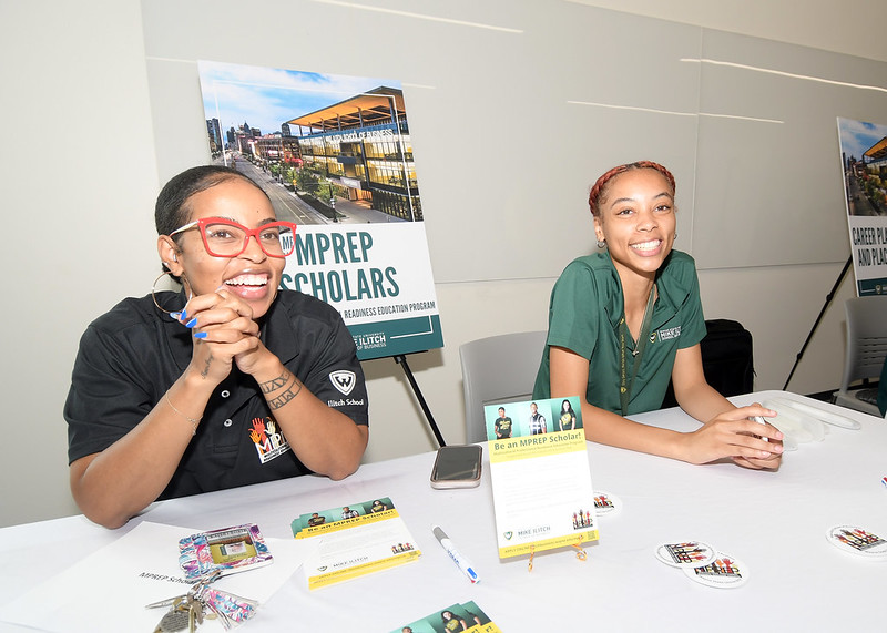 Two female representatives wearing MPREP polos sit at an MREP decorated table smiling