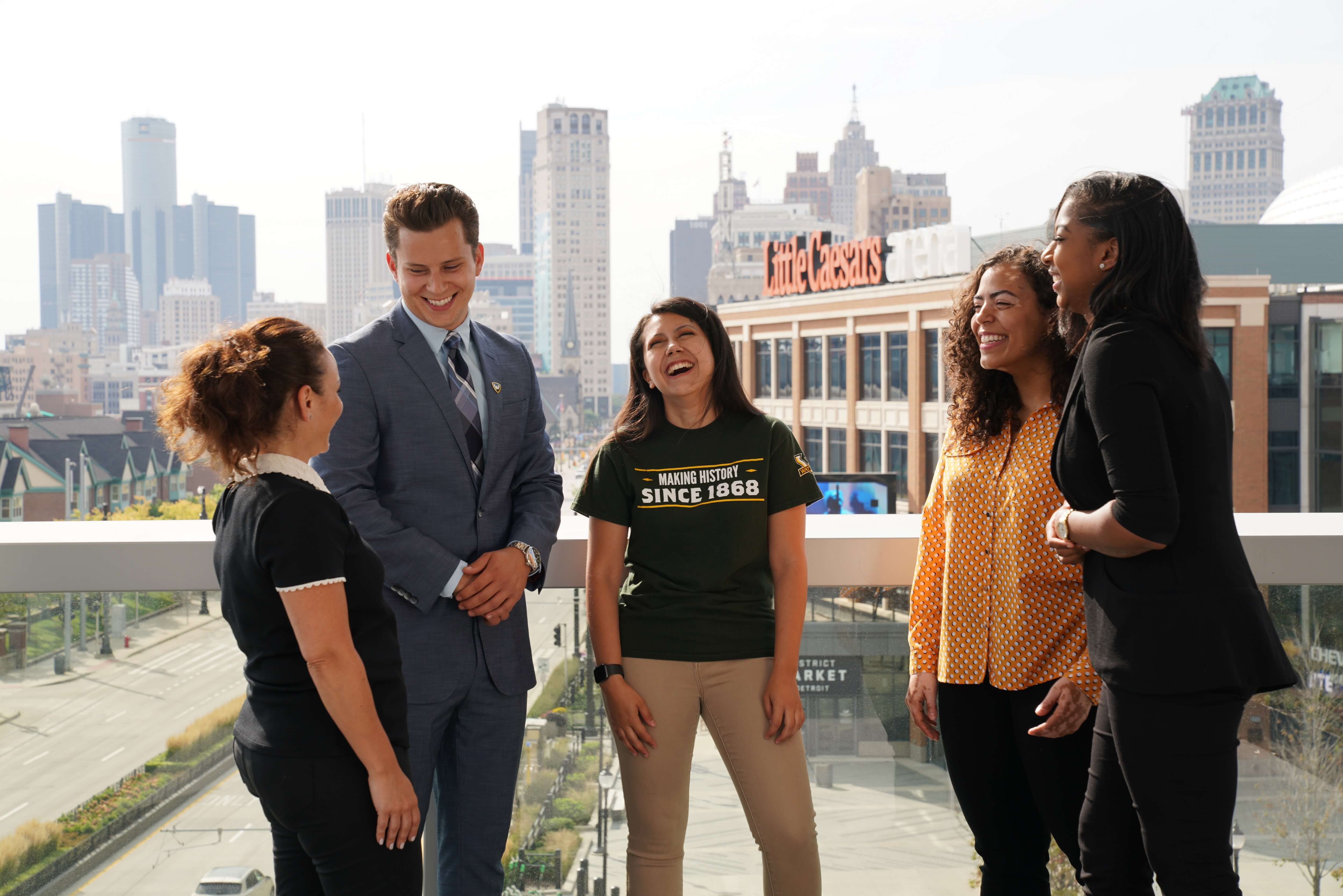 Five business students stand on Ilitch School&#039;s terrace looking at each other and laughing