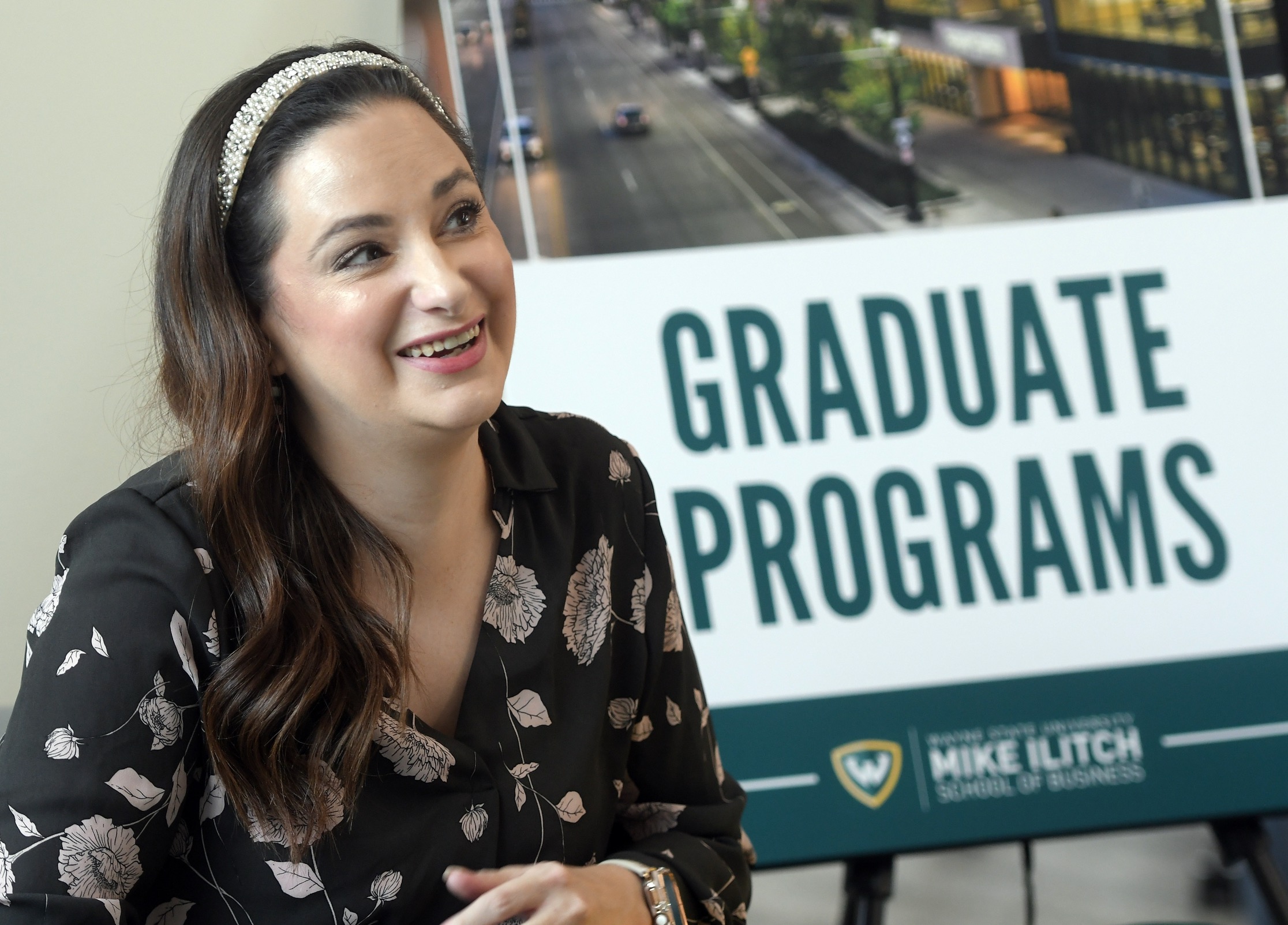 A female graduate advisor sits in front of a poster that says &quot;Graduate Programs&quot;