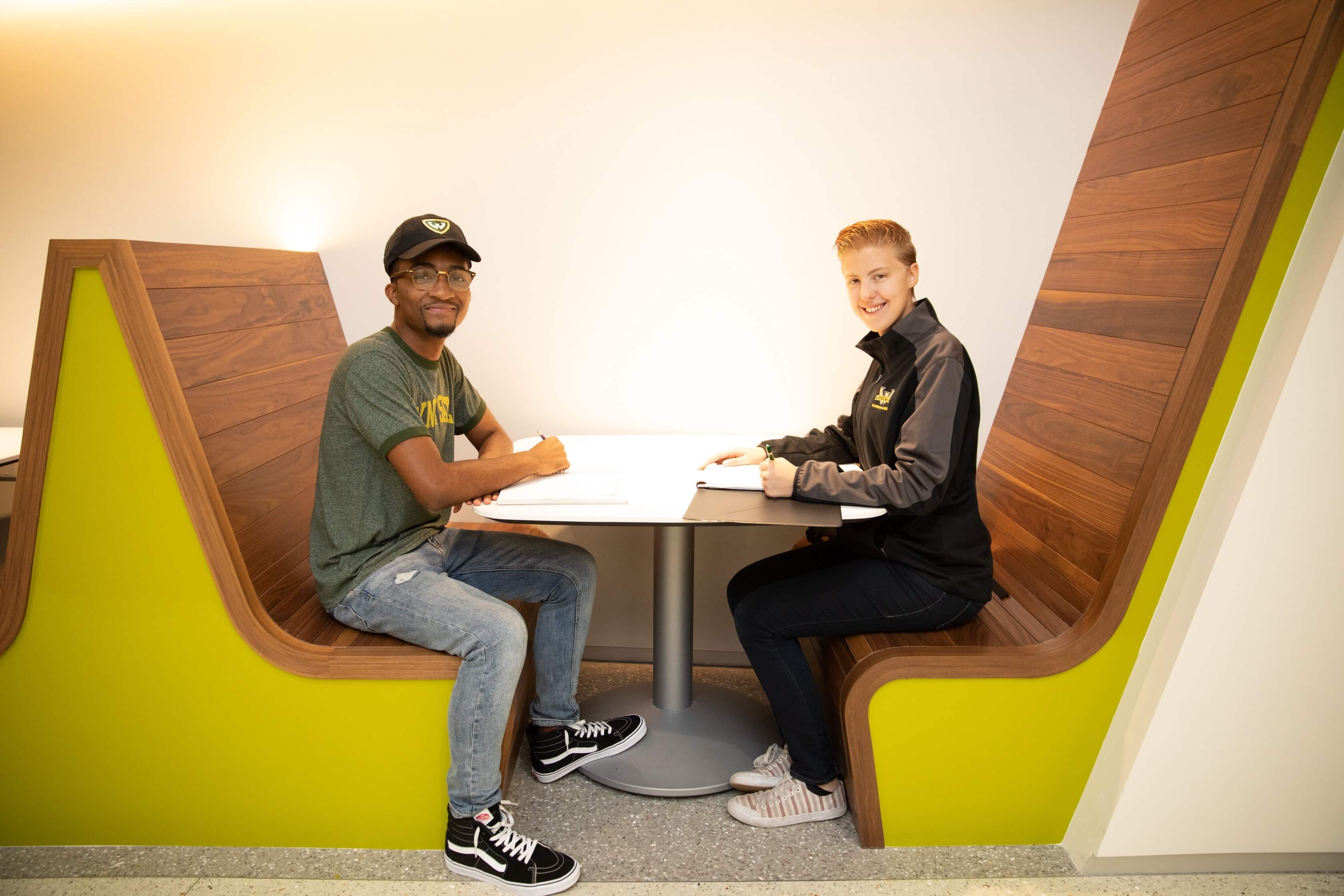 Two business students sit across from each other in booths at a table and are smiling