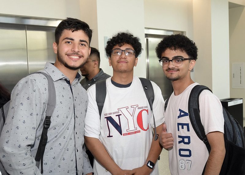 Three male business students wearing backpacks stand together posing in an Ilith School building in front of elevators