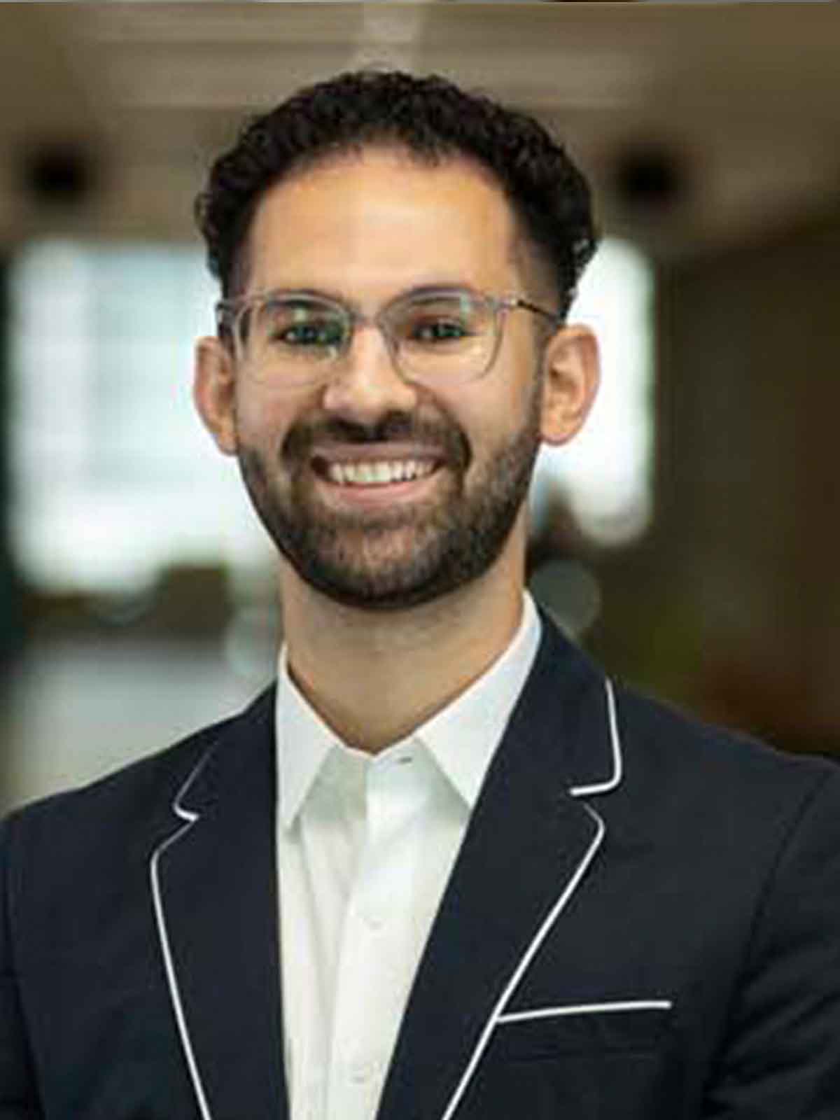 2021 Ilitch School MBA graduate, Simon Mourani, stands indoors and smiles for a headshot